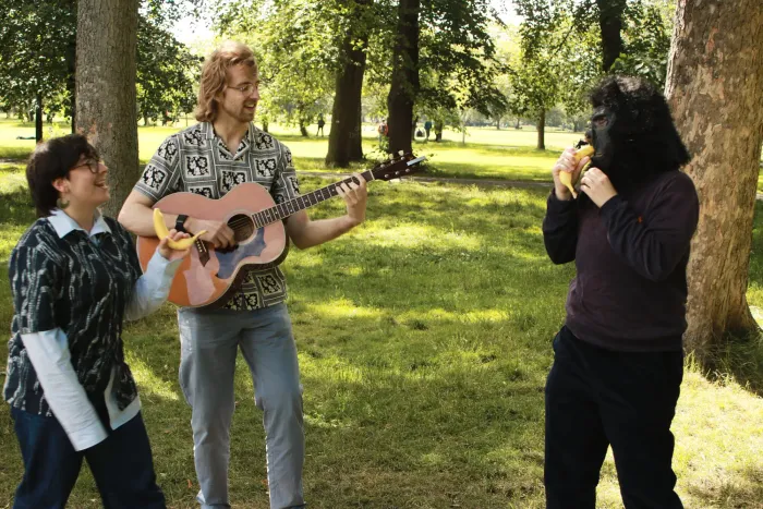 Mick playing guitar between while Bella and the monkey face off wielding bananas
