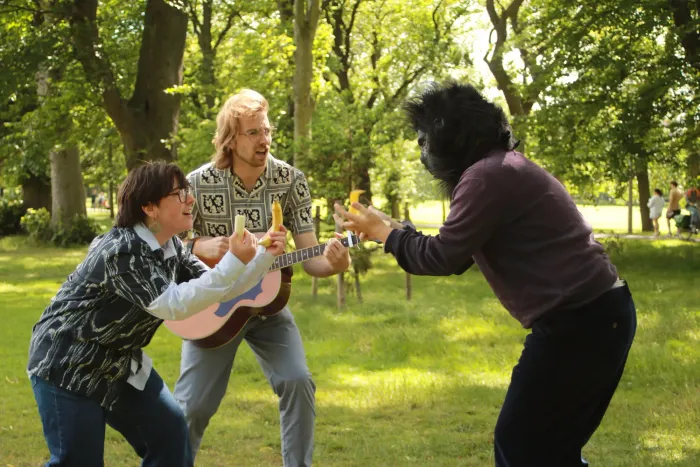 Mick playing guitar between while Bella and the monkey face off wielding bananas