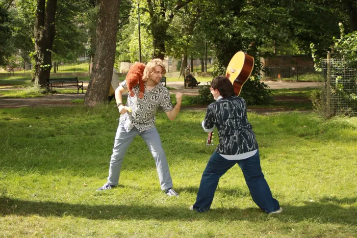 Mick, with a toy orangutan perched on one shoulder, squaring off across the grass against Bella, who has a guitar raised overhead