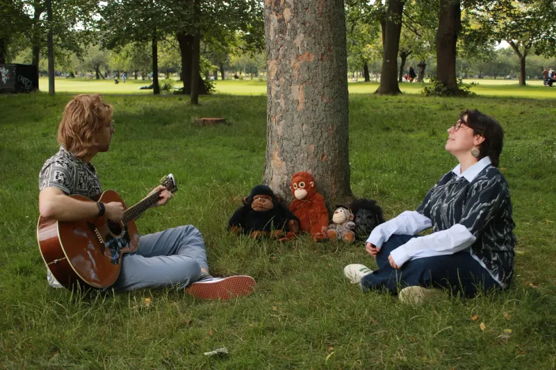 Mick playing guitar to a row of toy monkeys propped against a tree, Bella listening